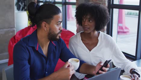 diverse couple sitting at a table in a cafe drinking coffee using laptop and talking