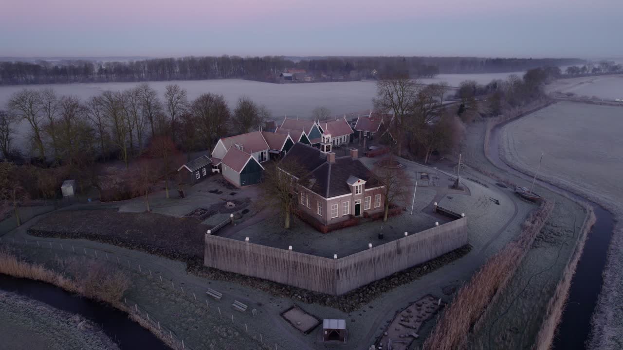 Východ slunce nad vesnicí s kostelem, domy a stromy, letecký pohled, Schokland, Nizozemsko