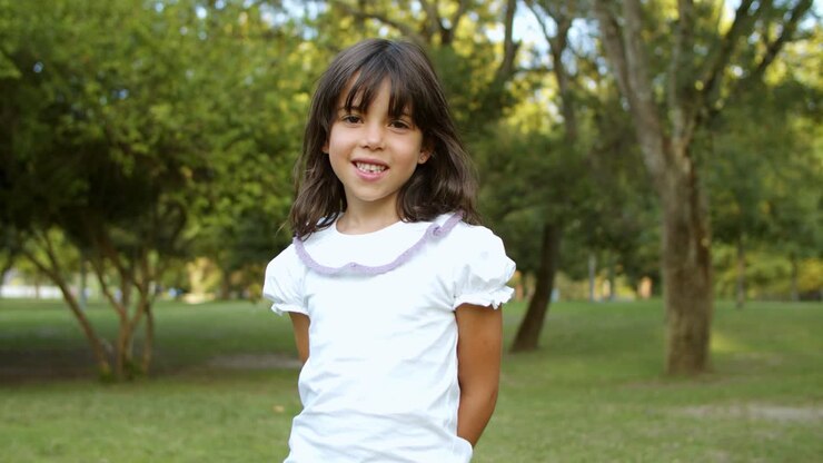 Niña pequeña y adorable de cabello negro de pie en un parque de la ciudad