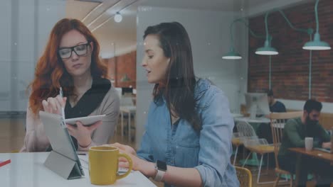 Animación-De-Gente-Caminando-Sobre-Dos-Empresarias-Caucásicas-Usando-Una-Tableta.