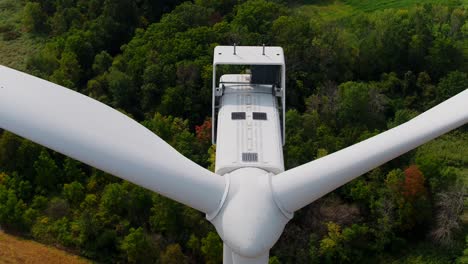 Inclinación-Aérea-De-Turbina-Eólica-Hacia-Abajo-Con-Bosque-Verde-Y-Campos-Detrás