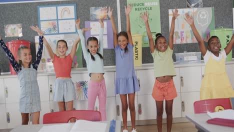 portrait of happy diverse schoolgirls raising hands in elementary school classroom in slow motion