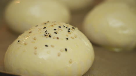 sprinkling sesame seeds over some silky and shiny burger buns ready to bake in the oven