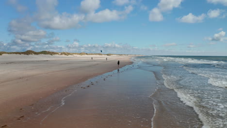 Dia--Und-Schwenkaufnahme-Von-Menschen,-Die-Einen-Sonnigen-Und-Windigen-Tag-Am-Strand-Verbringen.-Wellen-Waschen-Sand-An-Der-Küste.-Dänemark