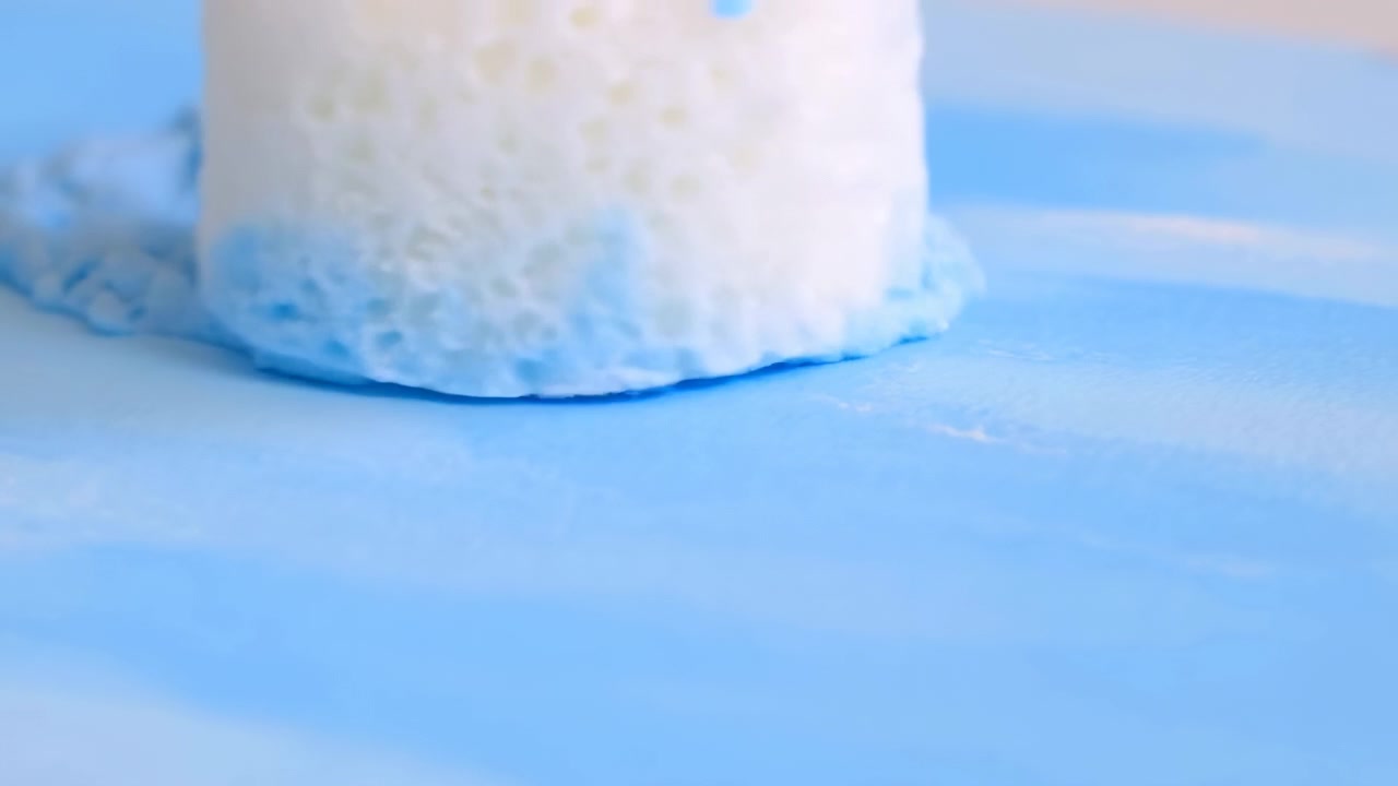 Rullo per pittura che preme su vernice fresca azzurro cielo, lasciando striature lucide su una superficie piana con bordo testurizzato, riflessi tenui e un aspetto da studio pulito e minimale