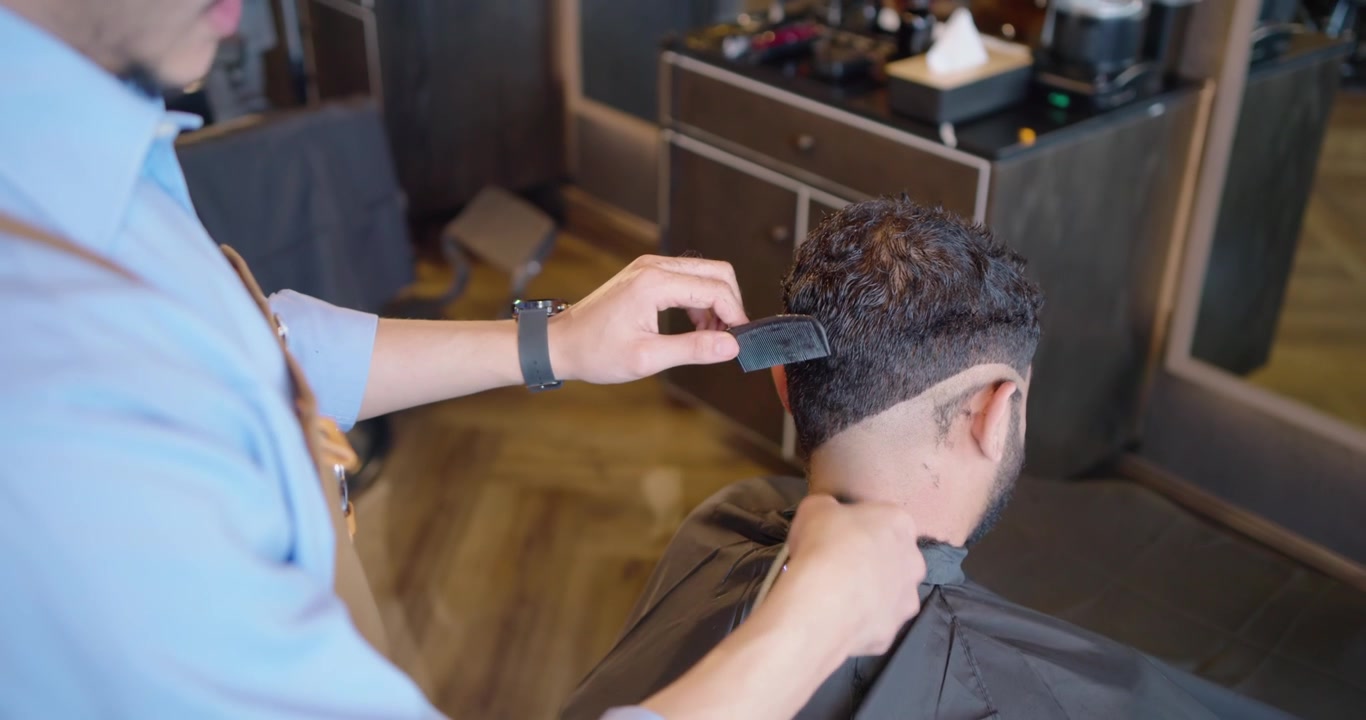 Afrikansk mandlig frisør lægger kappe på, trimmer mandlig kundes nakke med klippemaskine, former V-hals i salonen