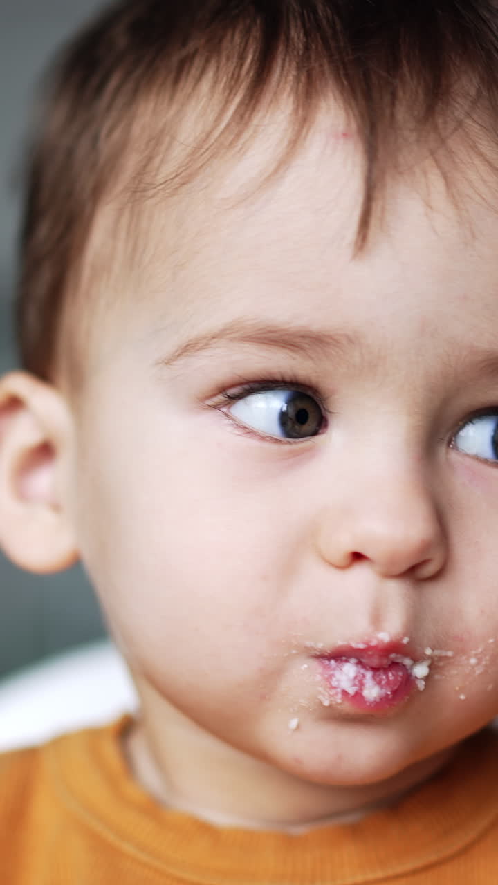 Cute dark-haired baby with smudged face opens mouth. Feeding a toddler from a spoon. Close up portrait. Vertical video