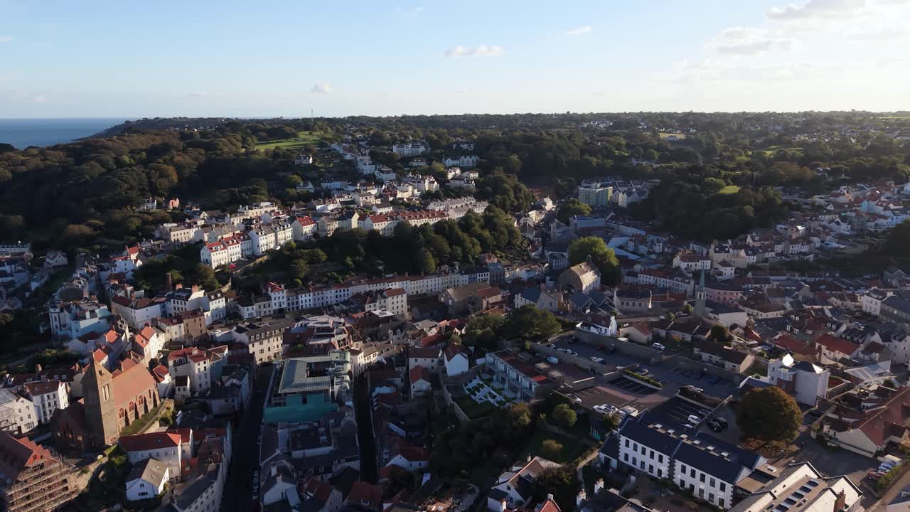 Very high drone footage over St Peter Port Guernsey flying south showing houses and buildings rising in terraces with the land a unique perspective with wonderful light