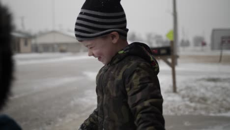 young boy standing outside in the snow smiles looking at the camera during christmas break in a small town in the midwest