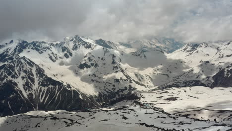 Air-flight-through-mountain-clouds-over-beautiful-snow-capped-peaks-of-mountains-and-glaciers.