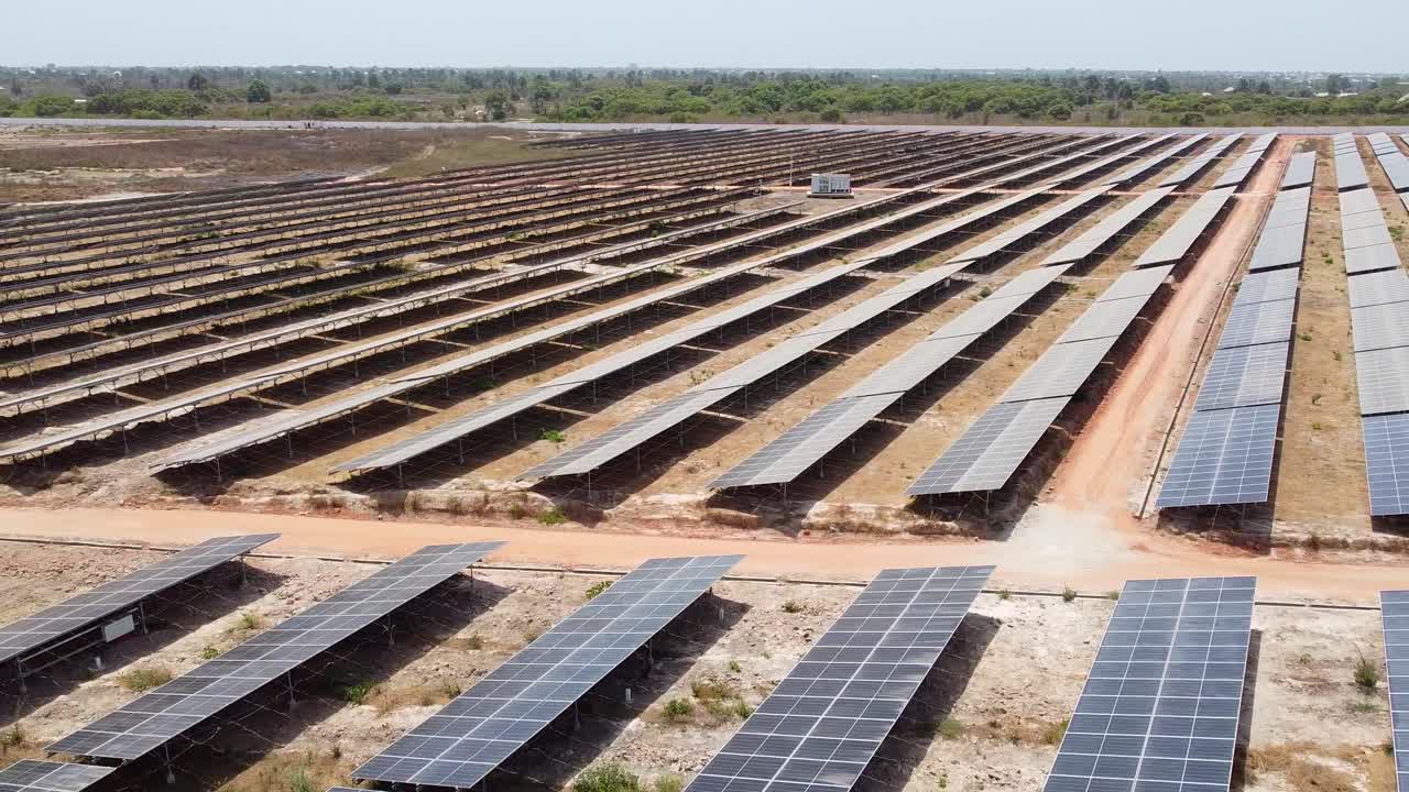 Low aerial drone view of solar energy farm with partially cleaned solar arrays in dusty African country
