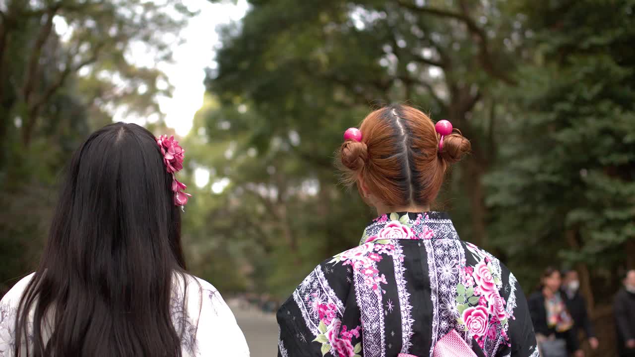 日本の神社で、花柄の着物を着た二人の女性が丁寧に頭を下げている後ろ姿。
