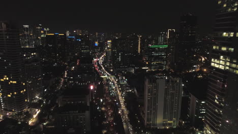 Distrito-De-Kuningan-De-Jakarta,-Vuelo-Nocturno,-Arriba-Y-Entre-La-Toma-Superior-Del-Edificio-De-La-Concurrida-Intersección-En-El-área-De-Kuningan,-Crea-Una-Tala-Urbana-Con-Mucho-Tráfico