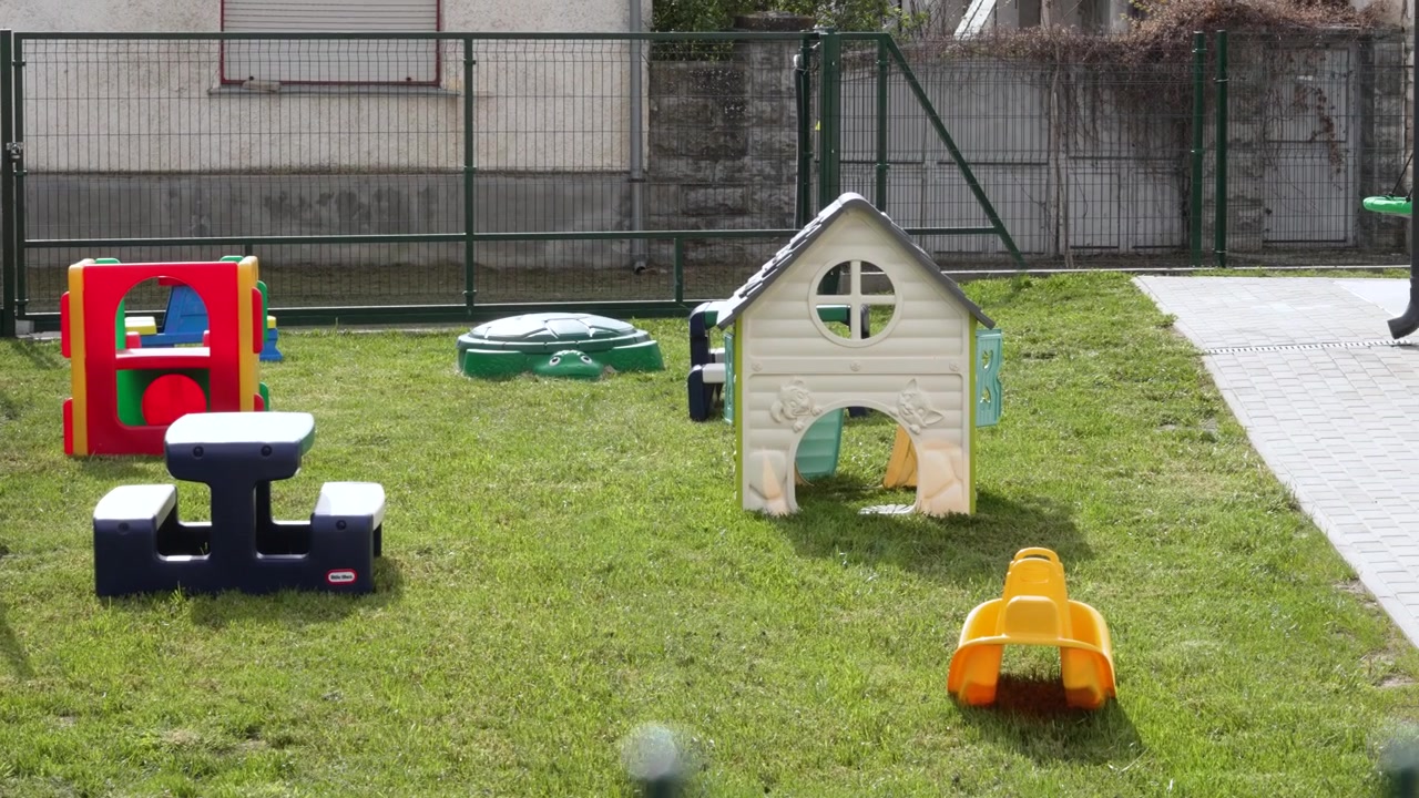 Mainan plastik berwarna-warni dan rumah bermain berdiri di atas rumput hijau di taman bermain umum modern