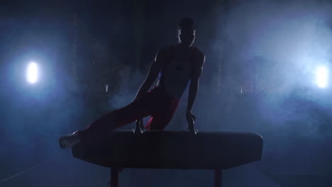 male-gymnast-athlete-performs-handstand-and-rotation-on-Pommel-horse-on-dark-background-and-smoke-in-slow-motion