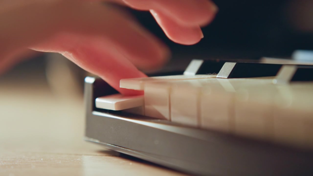 Close low-angle shot of portable keyboard with fingertip pressing white key, slight key depression, glossy black and white keys, warm bokeh lighting, tactile musical action and focused hand movement