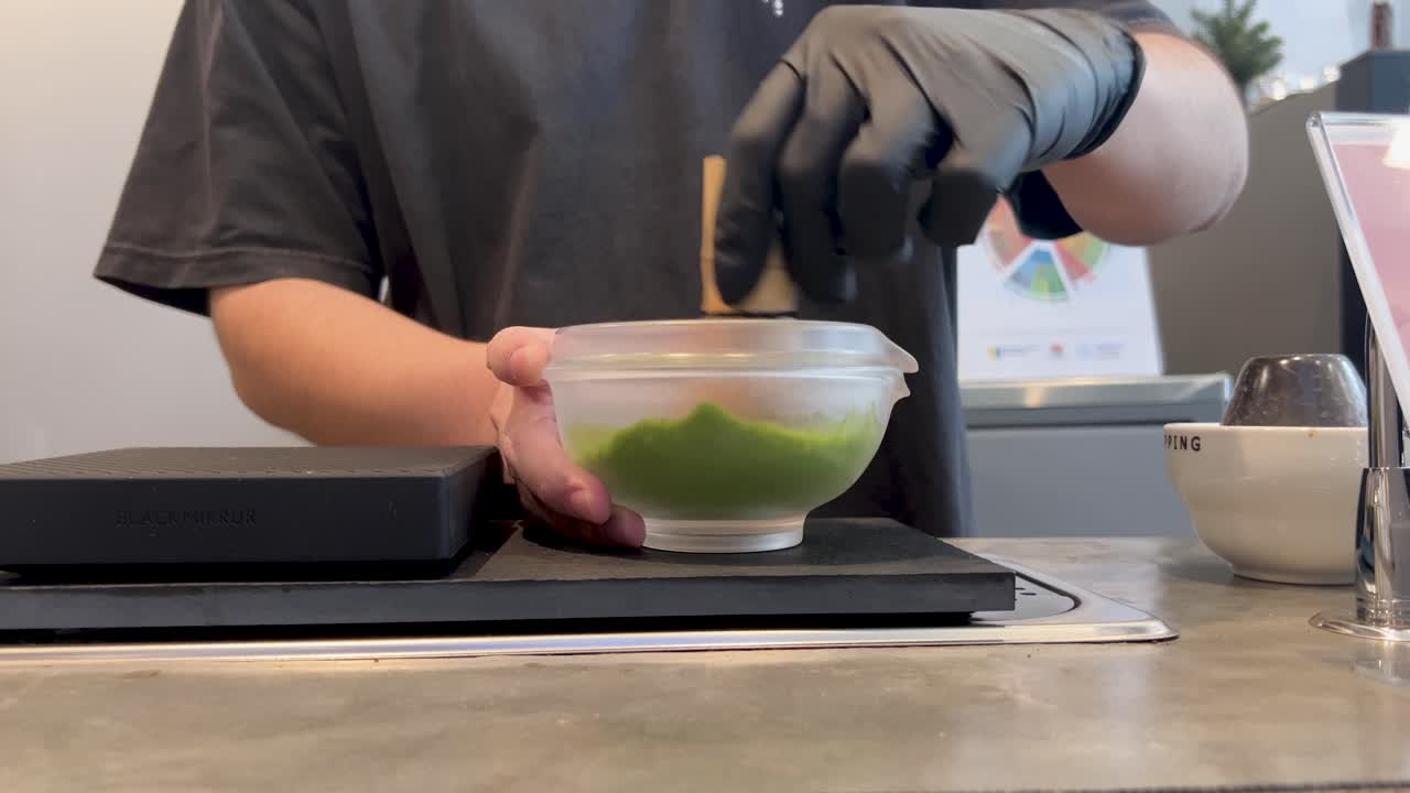 A barista skillfully mixes matcha tea in a modern Phuket cafe, using traditional techniques with precise movements and attention to detail