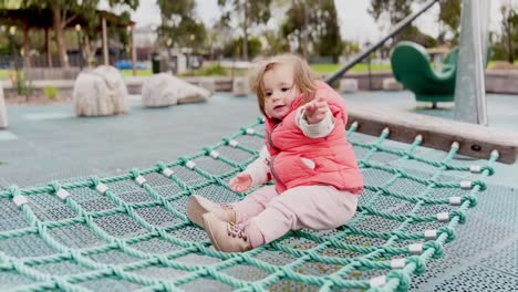 Caucasian-toddler-sitting-alone-on-a-rope-swing-with-bright-pink-vest