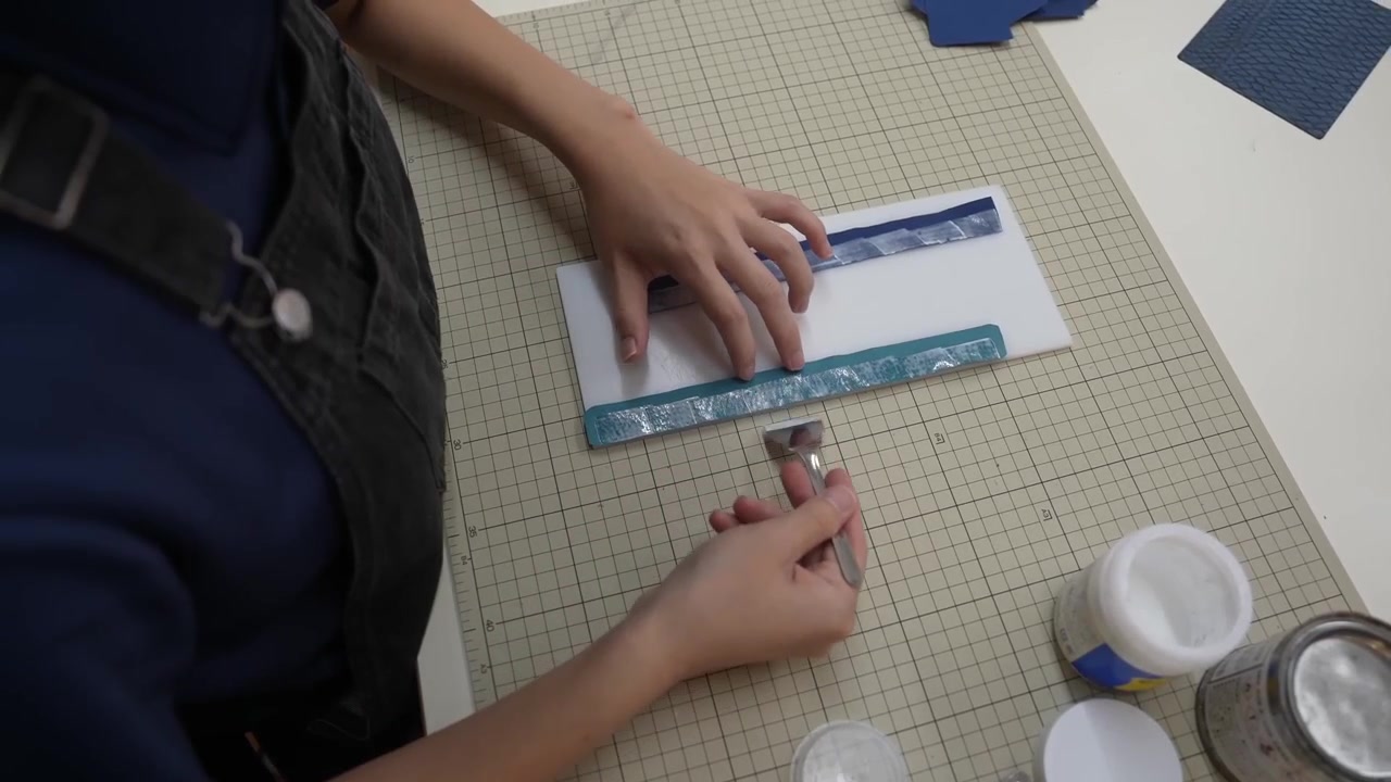 Hands cut leather strip along ruler edge using utility knife