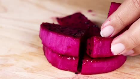a hand skillfully slices vibrant pink fruit into even pieces on a wooden board.