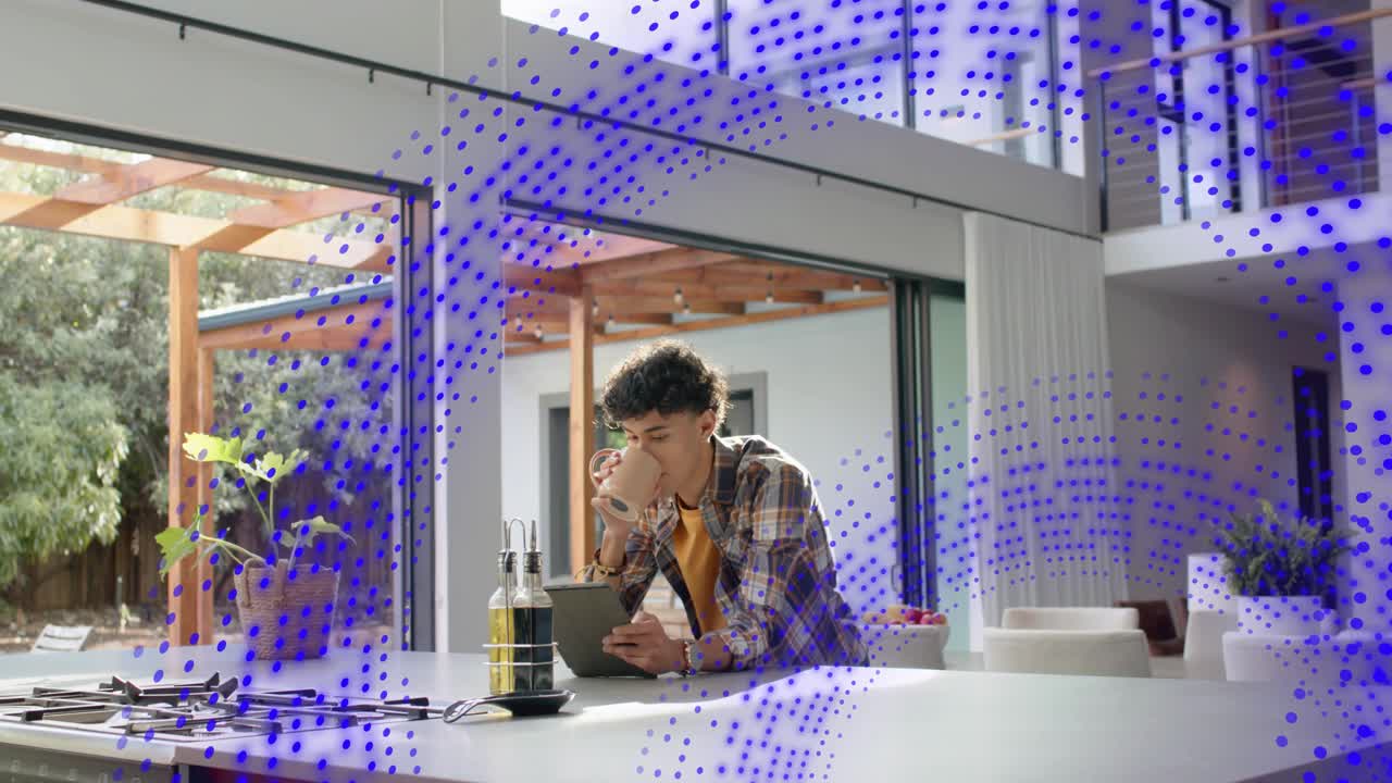 Man at kitchen island tapping tablet, causing blue dots growing and drifting while using technology