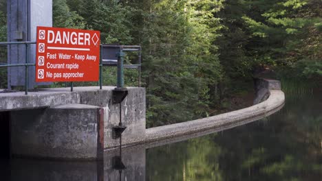 lake spillway dam infrastructure in nature landscape, danger sign and tree reflections