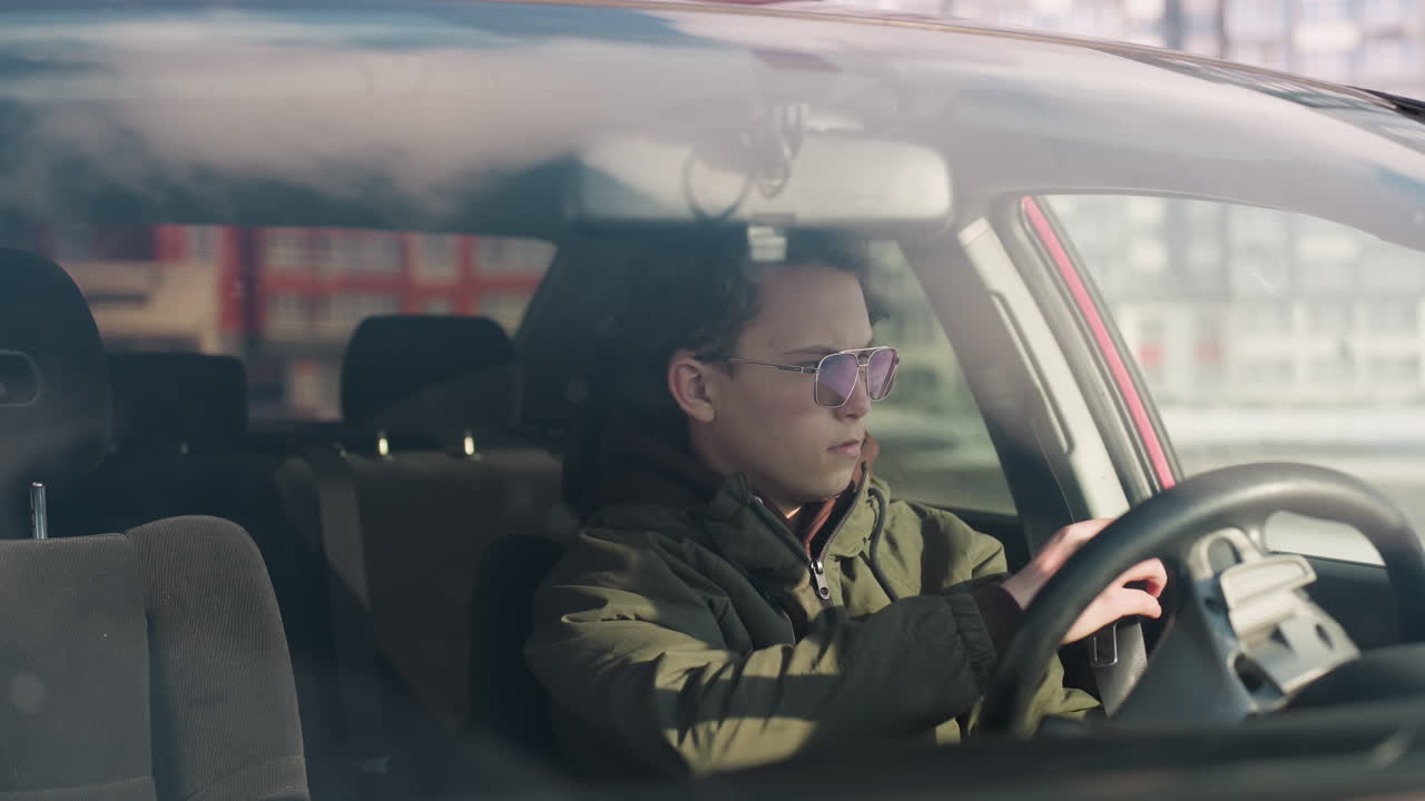 cab driver in parked winter vehicle unfastens seatbelt and grips steering wheel while focusing on device inside cabin with soft daylight and blurred urban background visible through window