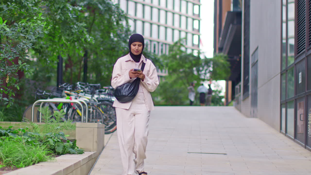 Muslim Businesswoman Wearing Hijab Going To Work Standing Outside Modern Office Looking At Mobile Phone 4
