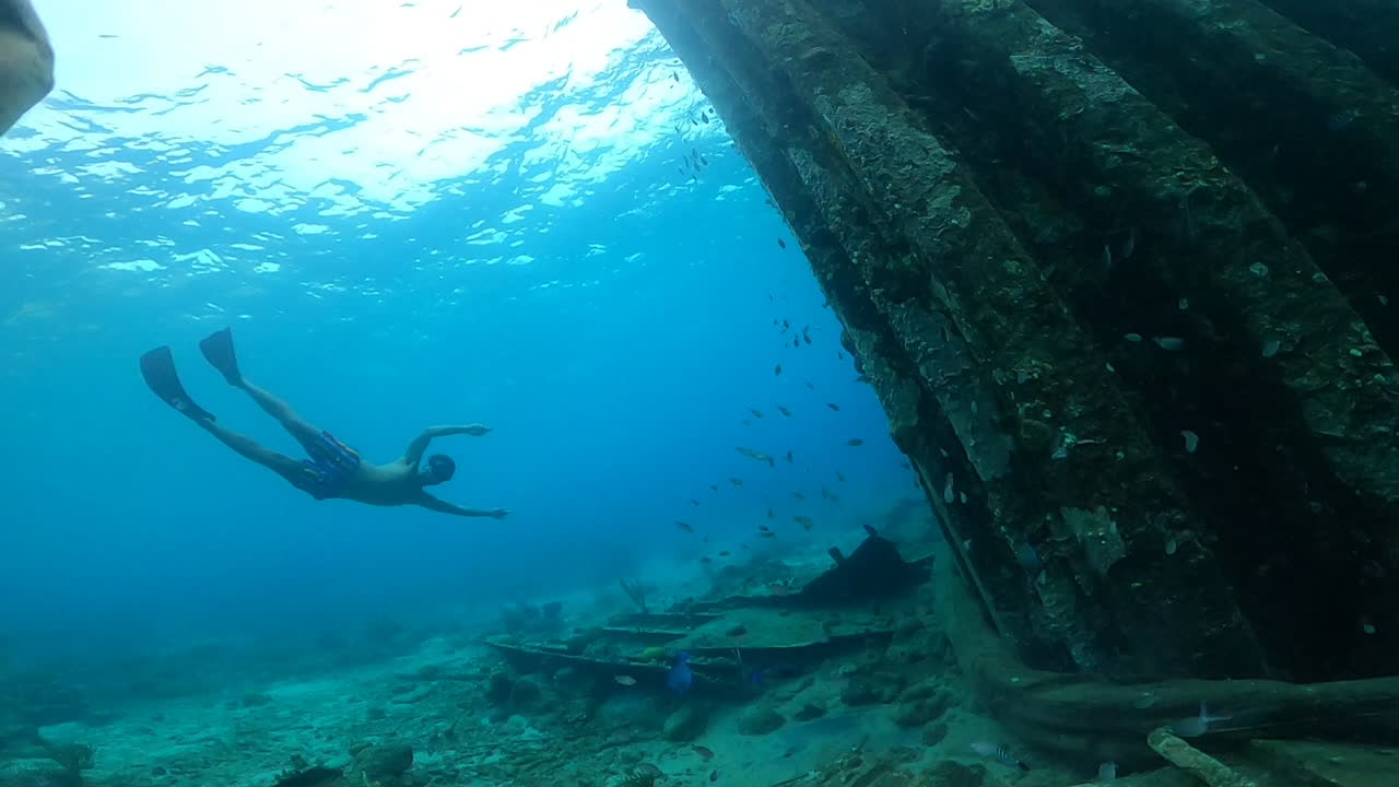 cámara lenta submarina de un hombre buceando libremente en un mar azul entre corales y muchos peces