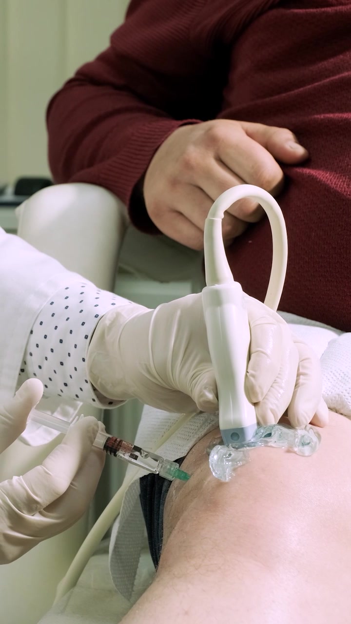 Medico che esegue un'iniezione ecoguidata nel ginocchio del paziente.
