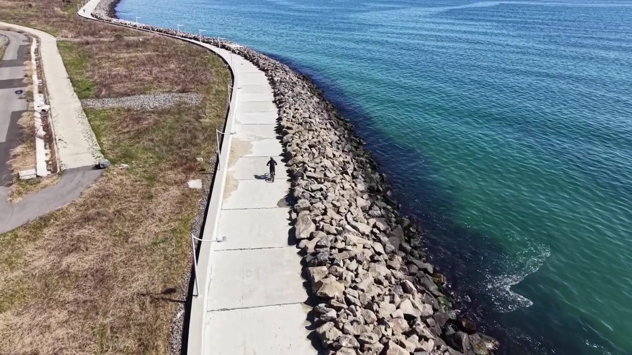Una persona pasea en bicicleta por un camino de concreto junto al agua, disfrutando de un día soleado cerca de la orilla en una zona costera