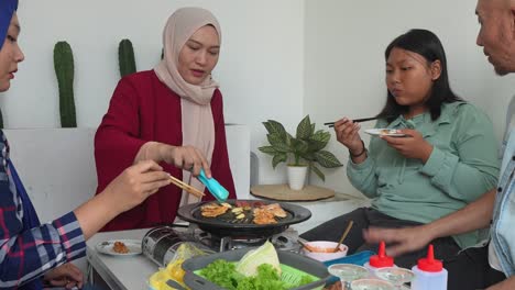 zoom out shot of happy asian muslim family eating korean barbeque grill together