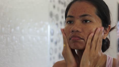 Close-up-shot-of-a-young-asian-woman-applying-acne-clearing-cleanser-on-her-chicks-and-forehead-trying-to-self-care-for-pustules-and-papules