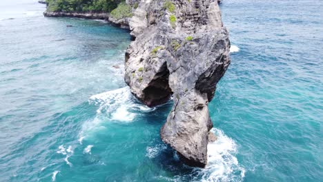 Natural-arch-Rock-formation-eroded-out-of-limestone-Nusa-Penida,-aerial-parallax-establish