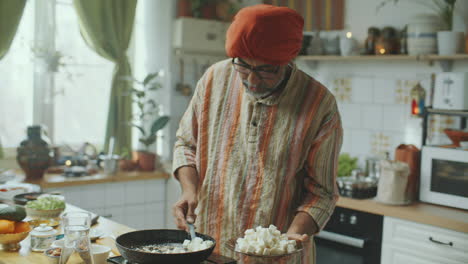 indian chef placing pan-fried paneer on plate and telling recipe in kitchen