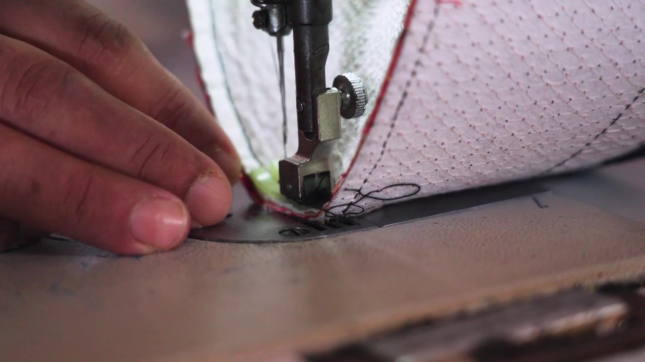 Close-up of a sewing machine stitching fabric for a traditional songkok in Malaysia. Skilled craftsmanship and precise hand guidance highlight cultural garment production and artisanal work.