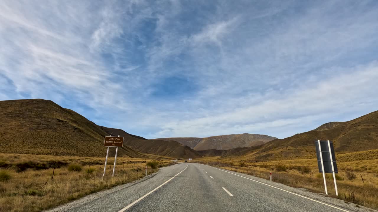 Aerial view of a road cutting through Lake Tekapo's rugged terrain under a vast, cloudy sky. Captures serene, expansive vistas