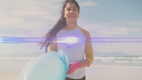 Animation-of-lights-over-smiling-hispanic-woman-picking-up-rubbish-from-beach