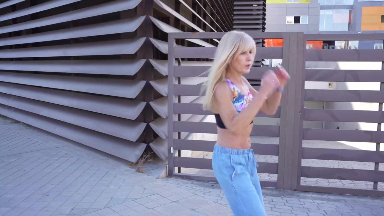 Uma mulher estilosa com um crop top colorido e jeans caminha ao ar livre perto de um edifício moderno da cidade.