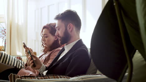 woman and man in formal wear using mobile phone and talking together while sitting on sofa