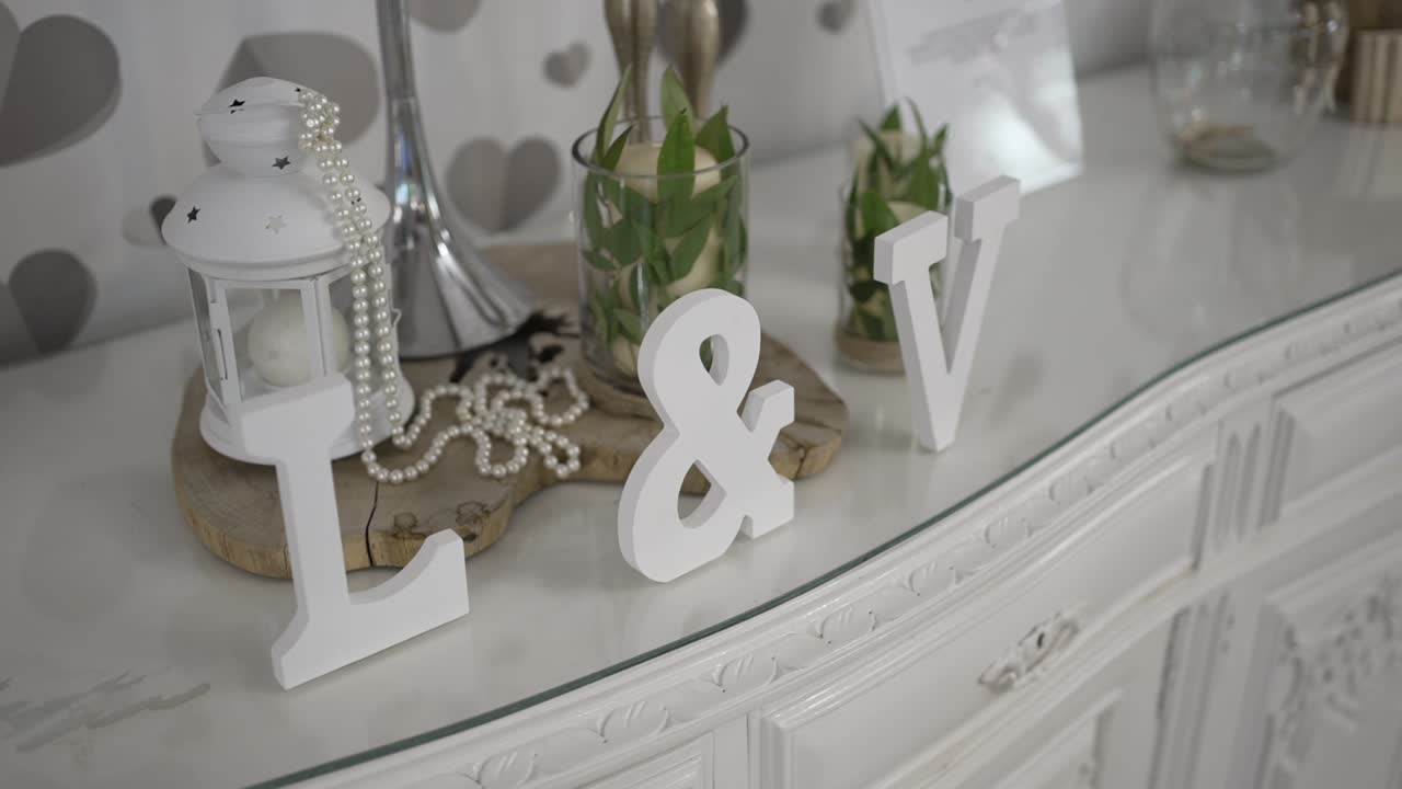 White decorative setup with initials L and V, pearl necklace, candle, and lantern