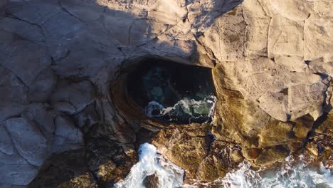 top down aerial of natural circular shaped pool, sea waves crashing against