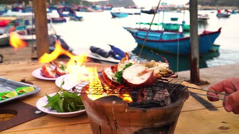 grilling lobster outdoors on clay charcoal stove in quiet fishing port, vietnam