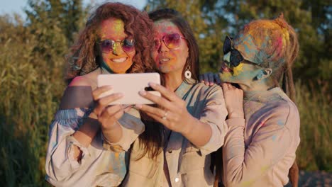 joyful young women posing for smartphone camera taking selfie with painted faces at holi celebration