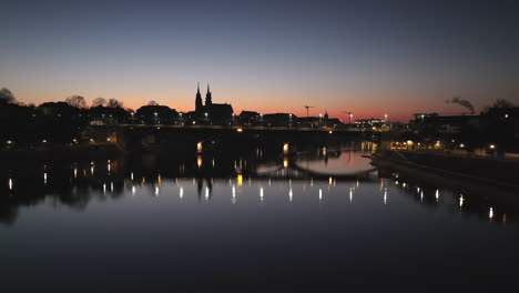 Toma-Panorámica-De-ángulo-Bajo-Con-Un-Reflejo-Del-Puente-Wettstein-En-El-Río-Rin-Y-En-El-Fondo-El-Horizonte-De-Basilea-Después-Del-Atardecer