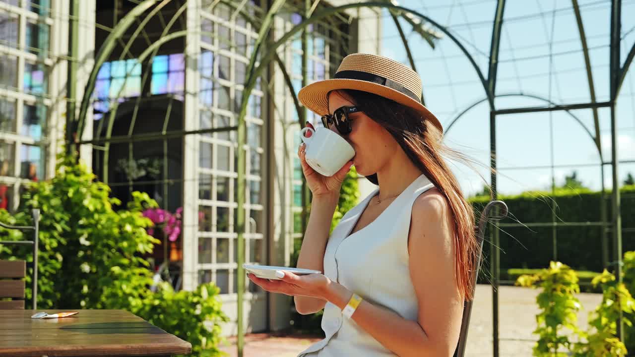 Slow motion, donna elegante che beve caffè mentre i suoi capelli ondeggiano nel vento estivo.