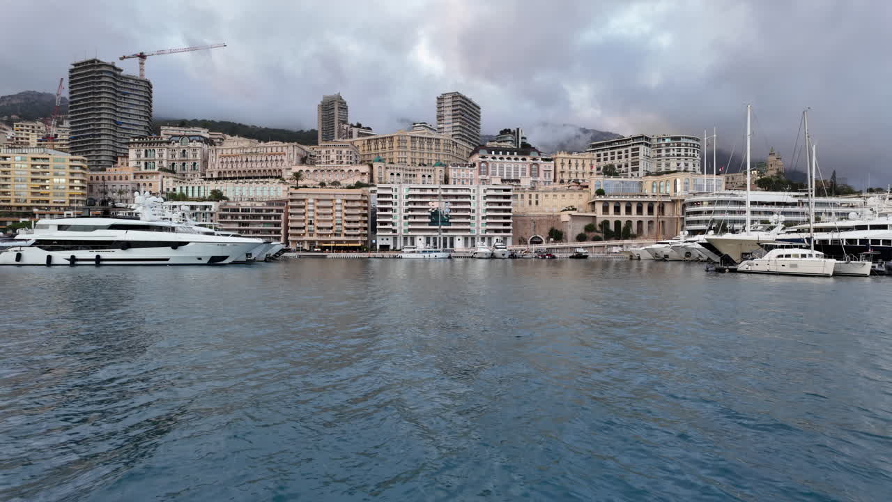La Condamine, Monaco - July 4, 2025: Row of sleek luxury yachts, docked in Port Hercules with the Monaco cityscape and misty hills in the background