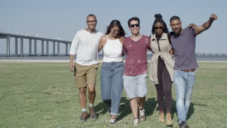 Gruppe-Lächelnder-Freunde,-Die-Sich-Beim-Spaziergang-Auf-Der-Wiese-Umarmen