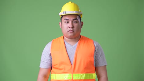 젊은 잘생긴 과체중 아시아인 남자 건설 노동자 초록색 배경