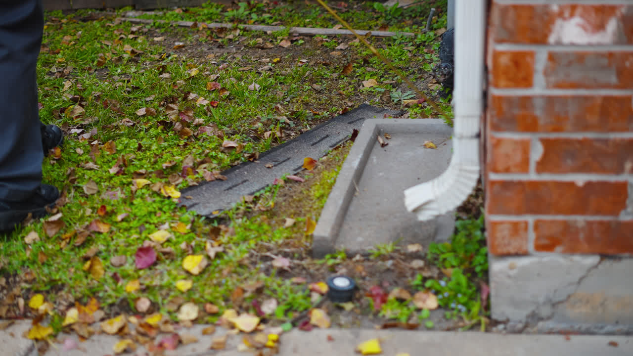 Pest control treatment applied along exterior base of brick house foundation around edge of gutter outflow pipe
